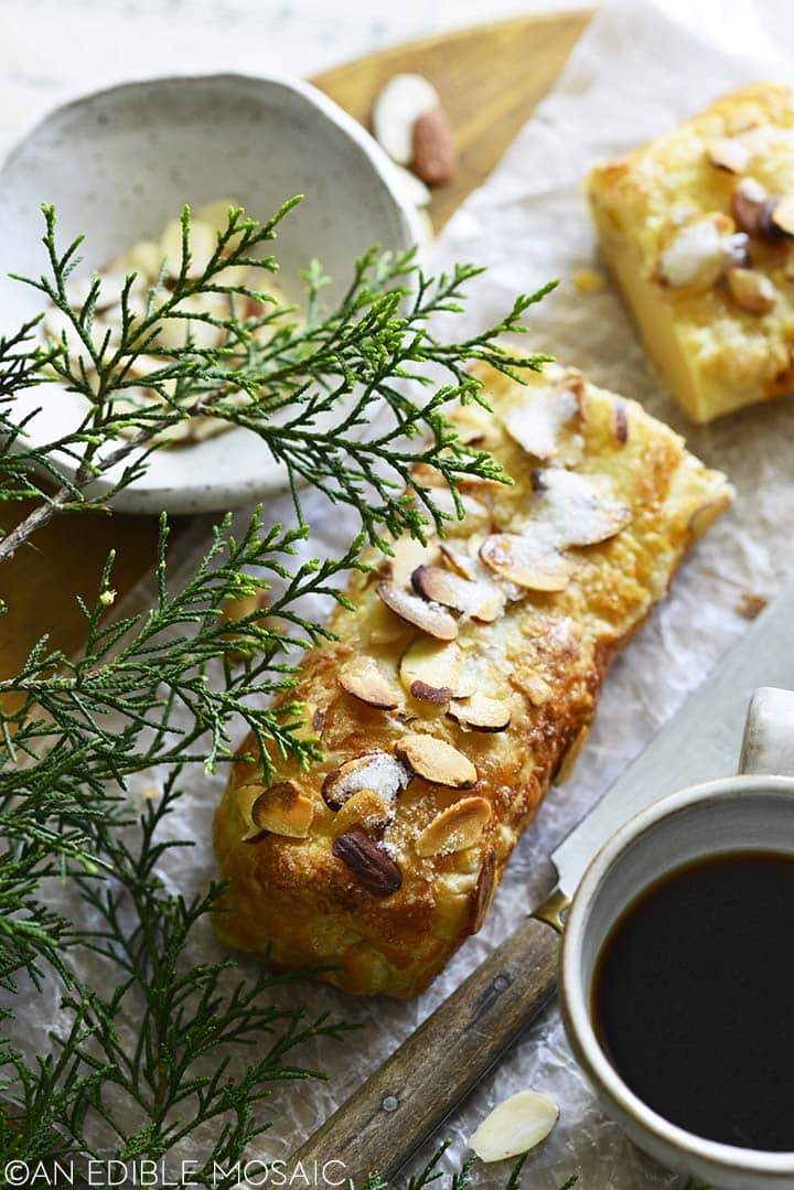 Marzipan filled log pastry with coffee and evergreen plant in foreground.