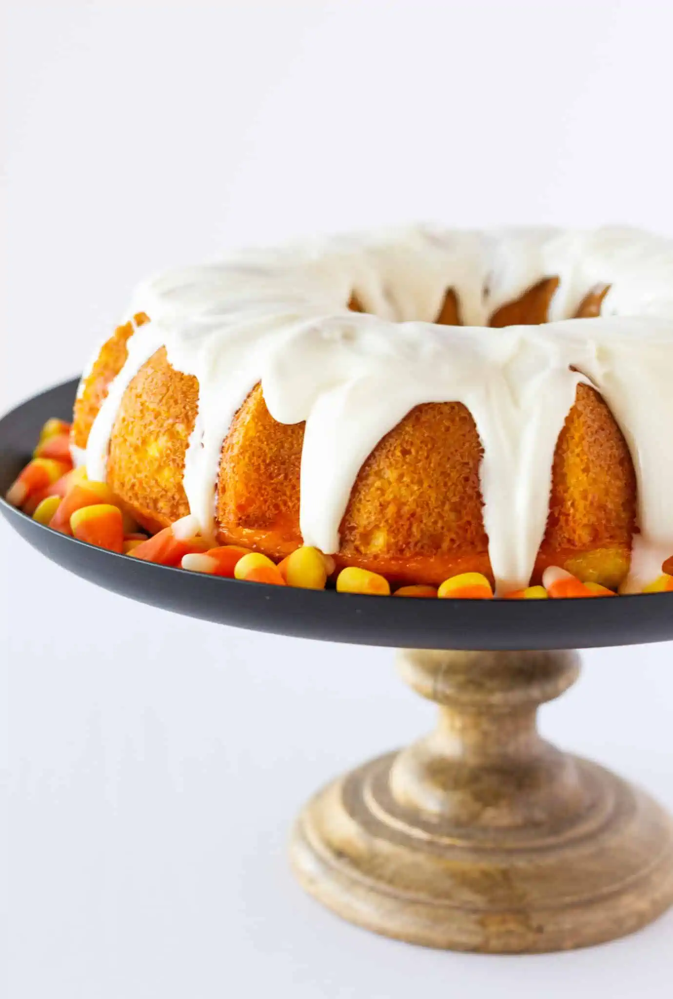 Bundt cake on a pan with candy corn on a stand with a white background.