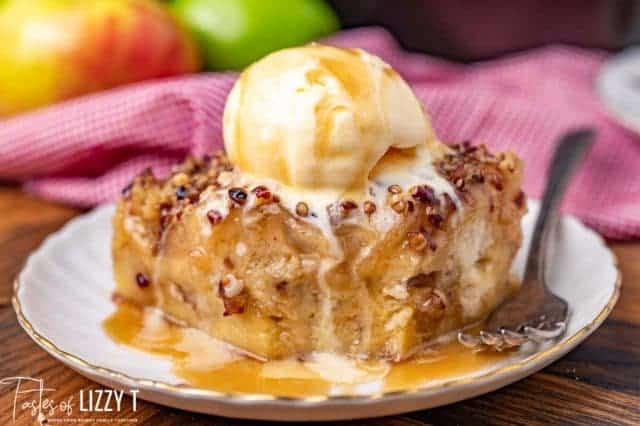 Caramel apple bread pudding on white plate with ice cream and caramel sauce on top.