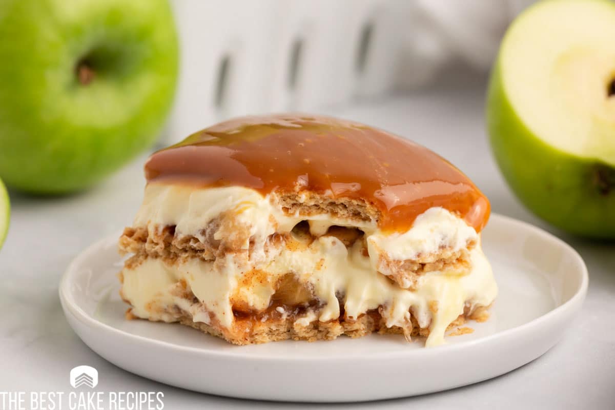 caramel apple eclair cake on white plate with green apples in the background.