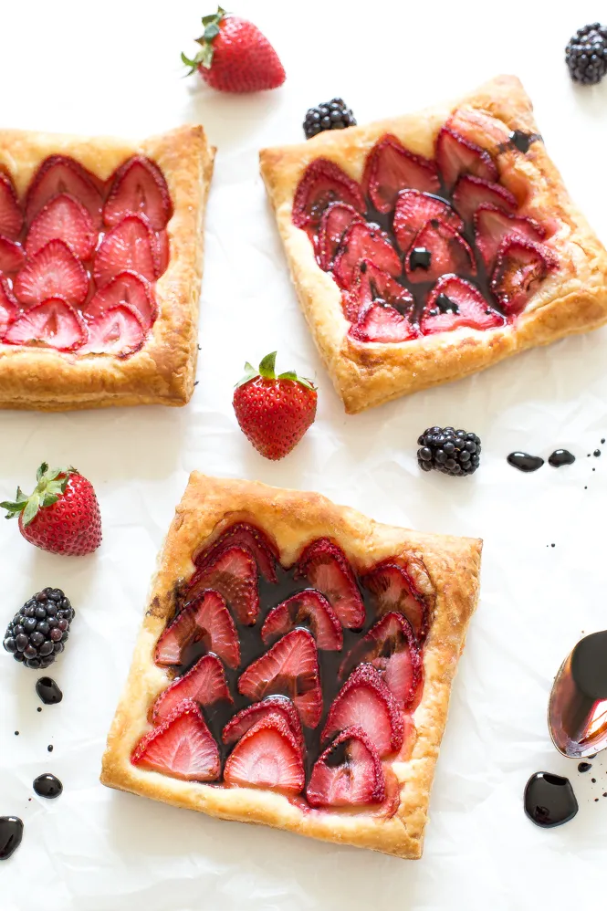 Strawberry tarts with strawberries and blackberries on a parchment paper.