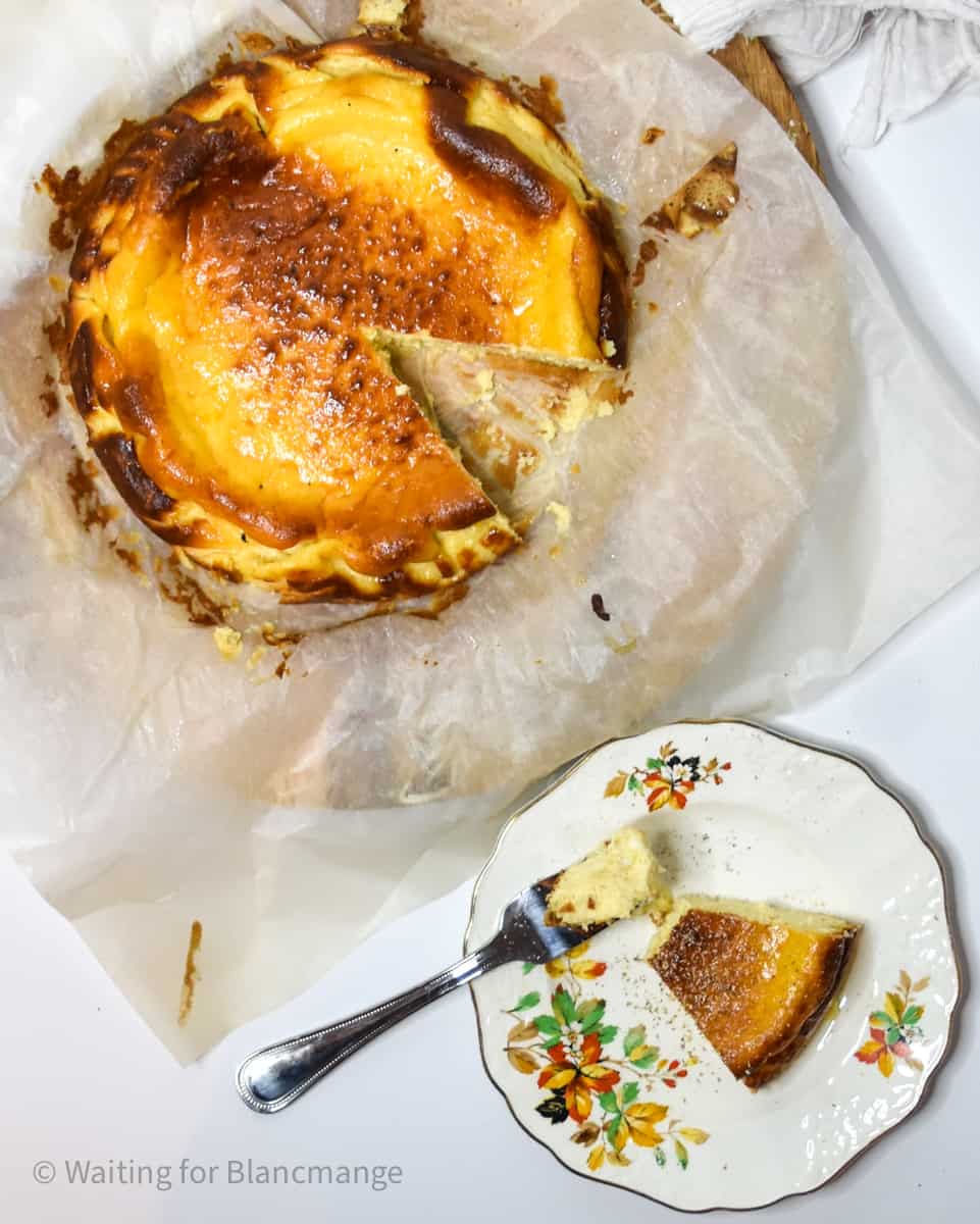 Eggnog Basque cheesecake on parchment paper with slice on a festive white plate.