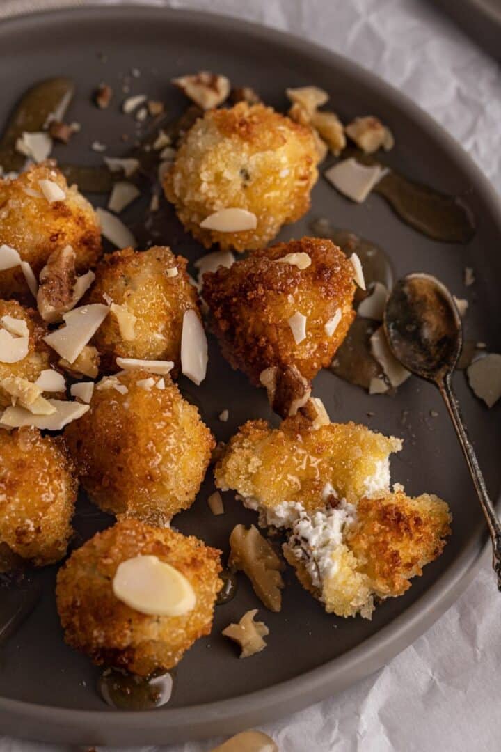 Goat cheese croquettes on a grey plate with chopped nuts and spoon with honey drizzle.