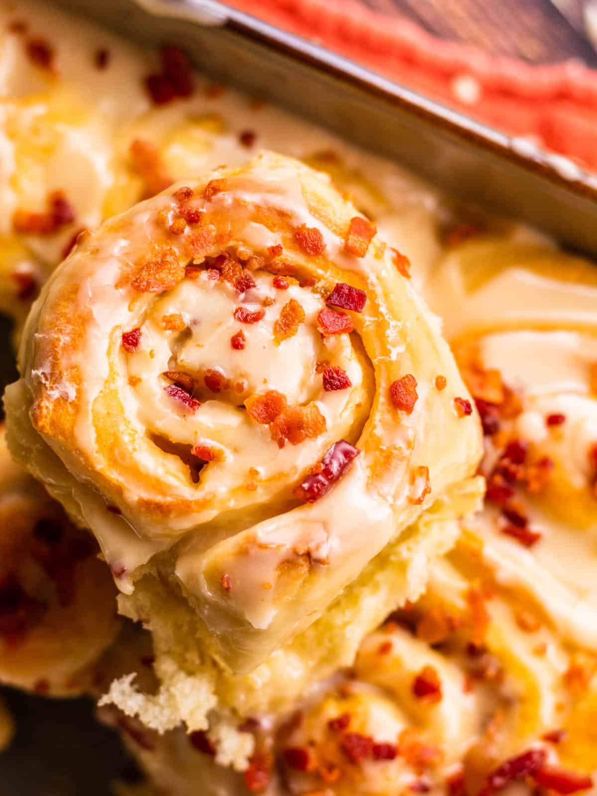 Maple bacon cinnamon roll in hand with more in pan background.