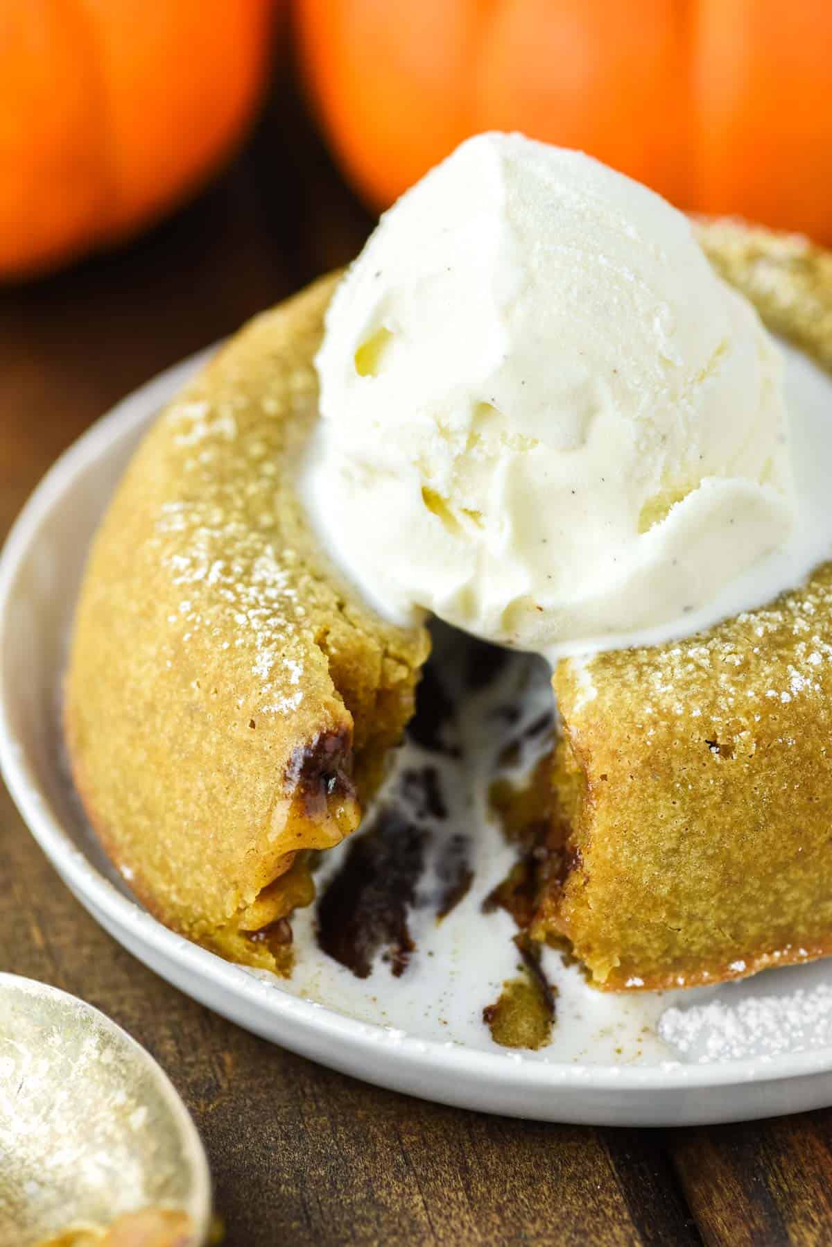Pumpkin lava cake with scoop of vanilla ice cream on white plate and wooden background.