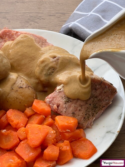 Bacon chops with potatoes and carrots, smothered in gravy on a white plate.