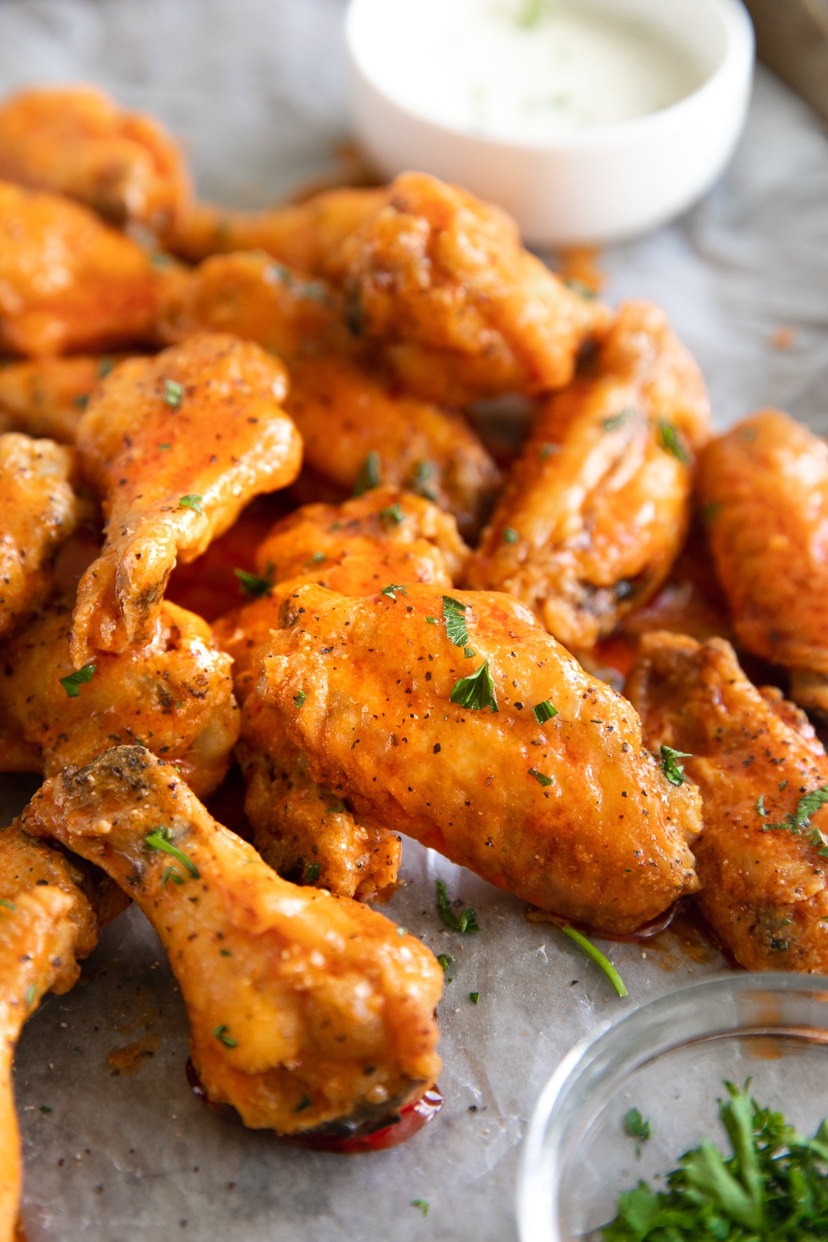 Pile of Buffalo wings sprinkled with herbs on parchment.