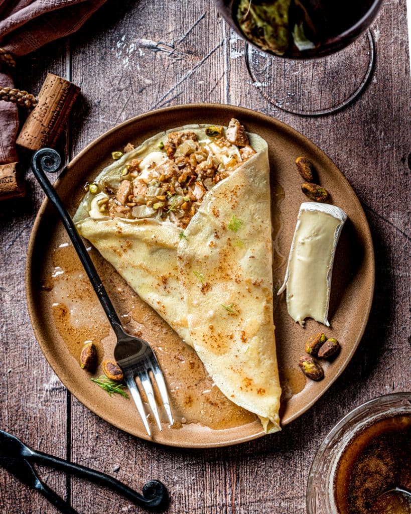 Brie, chicken, and pistachio filled crepe on a plate with fork.