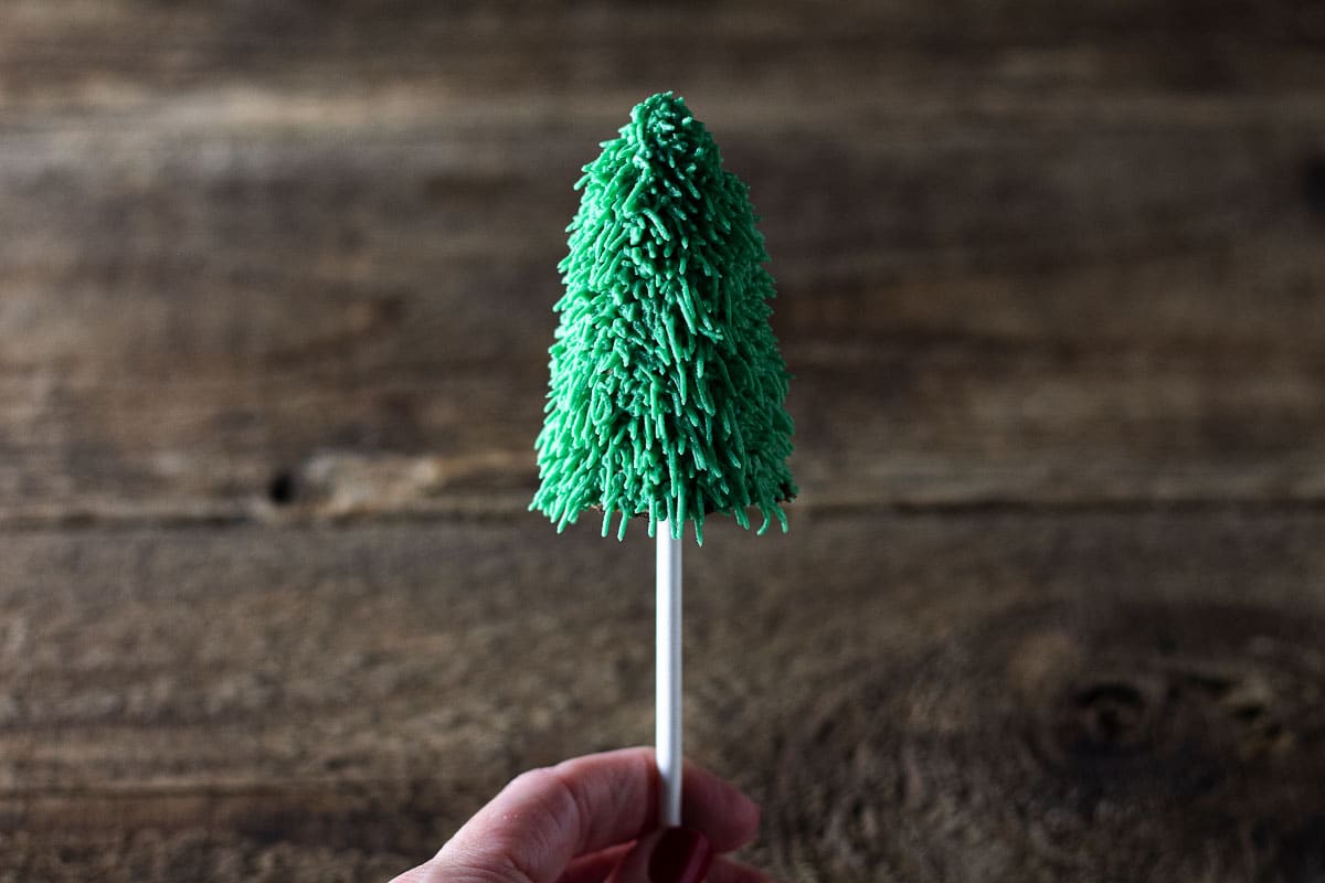 Completely frosted Christmas cake pops held in hand.