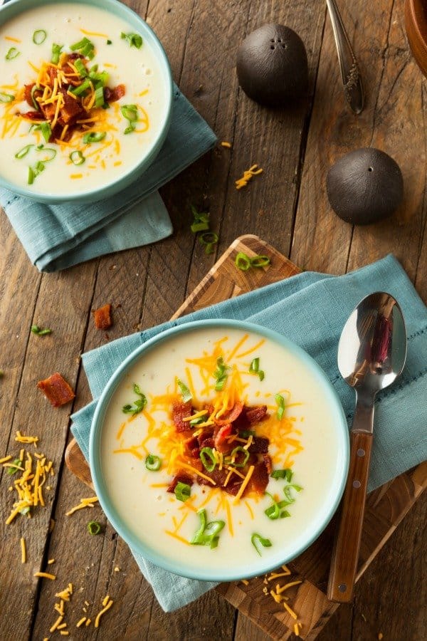 Two servings of loaded crockpot potato soup in bowls with salt and pepper shakers.