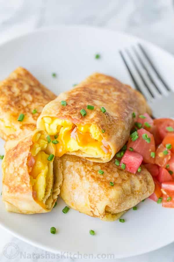 Egg, ham, and cheese crepes on a white plate with fork.