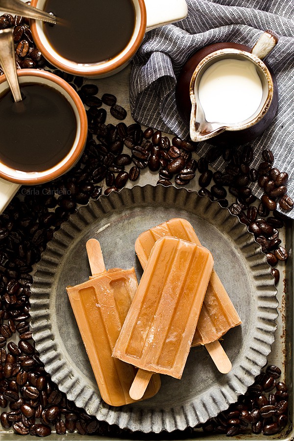 Iced coffee popsicles on serving tray with coffee and cream in the background.