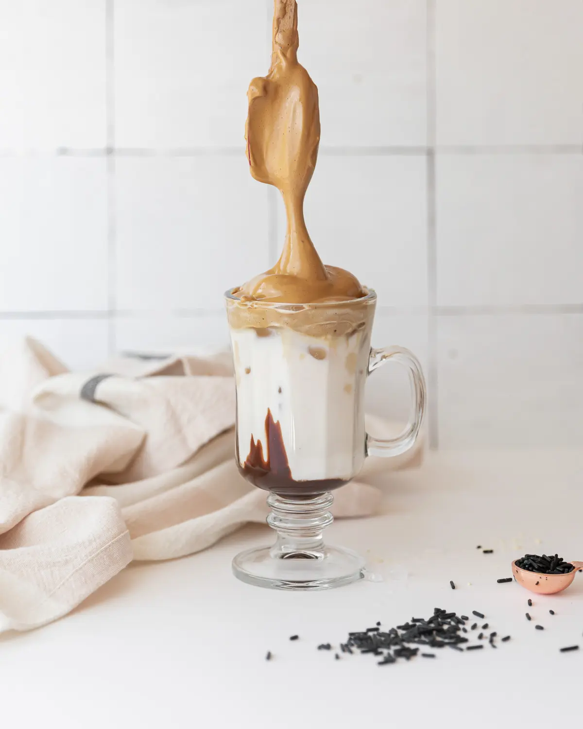 Spoon adding dalgona whipped coffee to a glass.