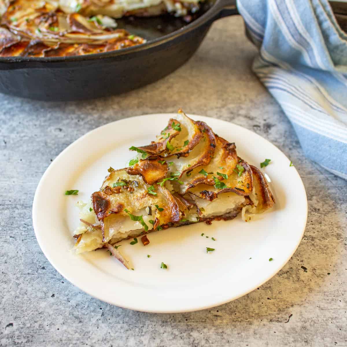 Slice of potato galette on a white plate with cast iron pan in the background.