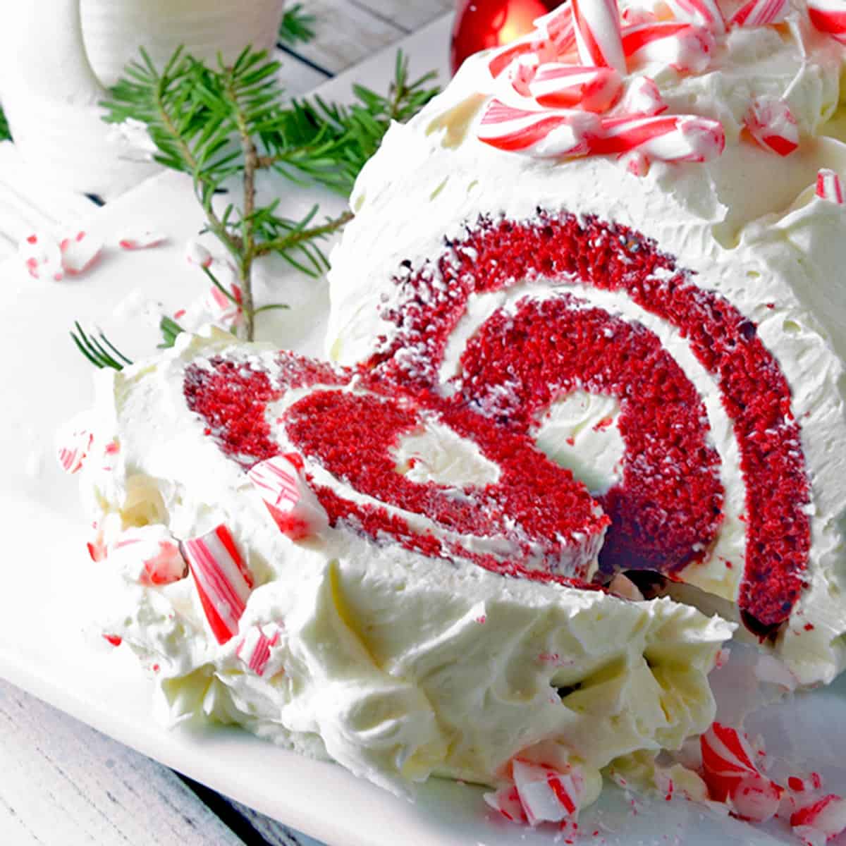 Red velvet cake roll with peppermint candy on white serving platter.