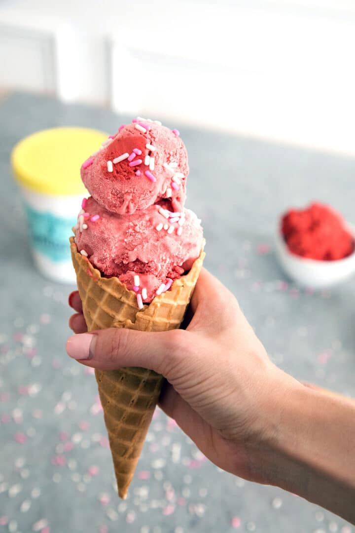 Red velvet cookie dough ice cream in a cone held in hand.
