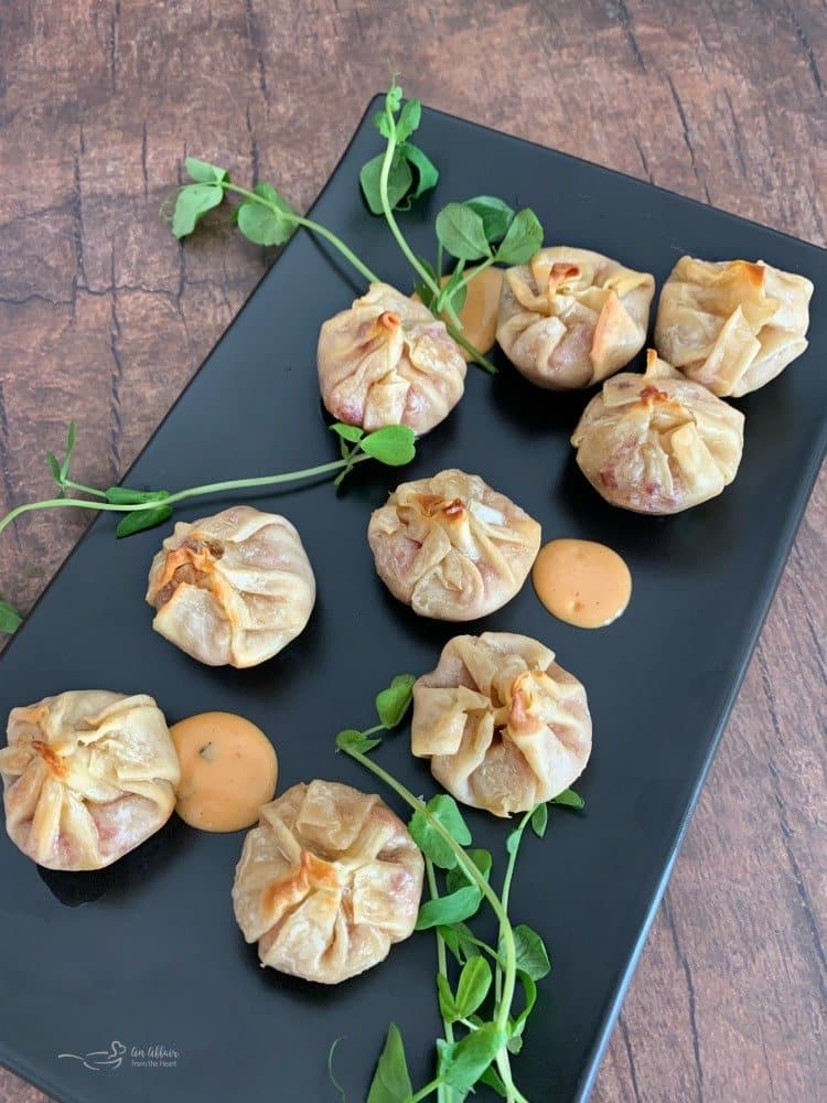 Reuben wonton purses with thousand island dressing on a black plate.