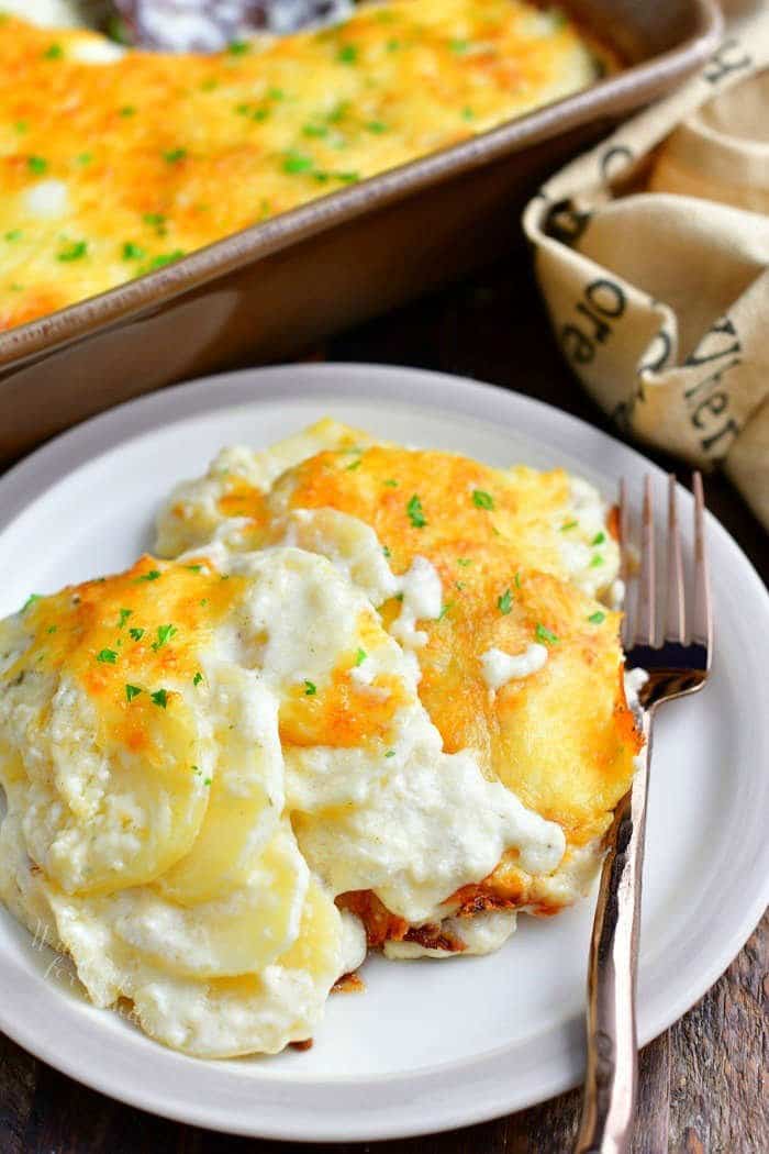 Scalloped potatoes serving with fork on a small white plate with more in baking dish in background.