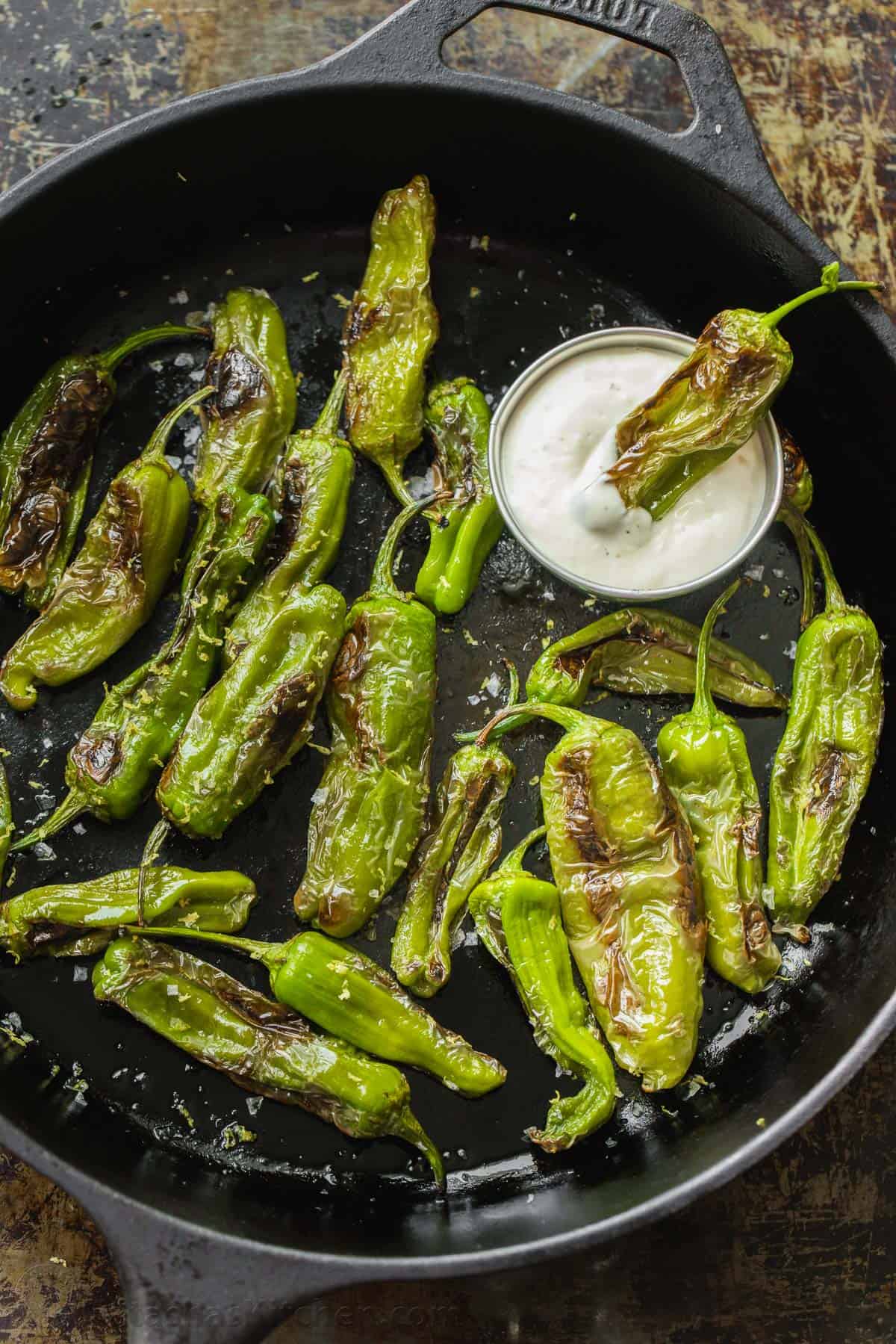 Blistered shishito peppers with dipping sauce in a cast iron pan.