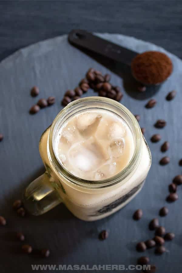 Homemade vanilla iced coffee in a mason jar with coffee beans.