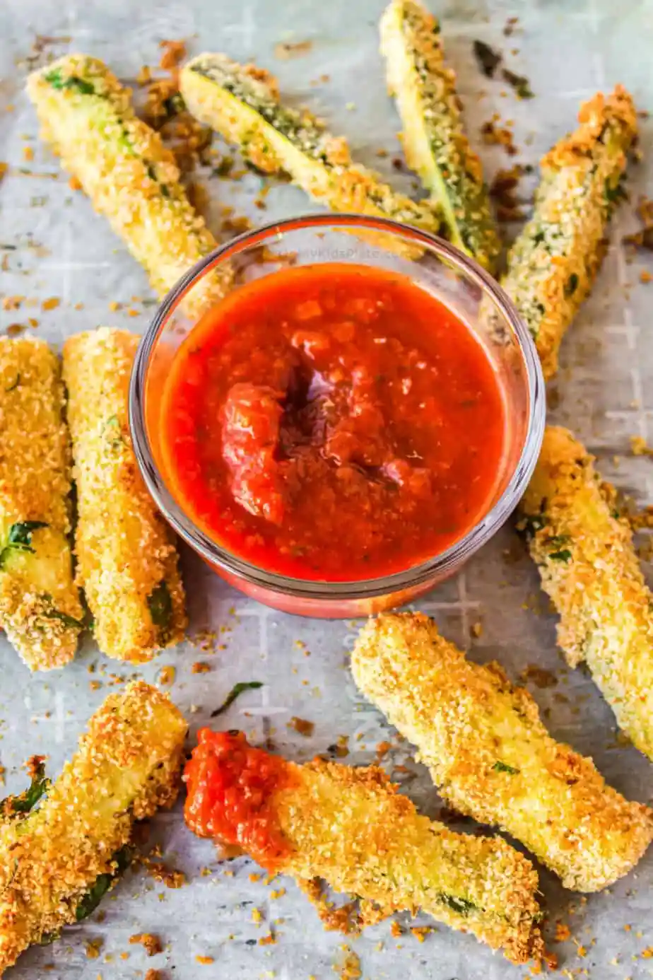Air fryer zucchini fries on parchment with dipping sauce.