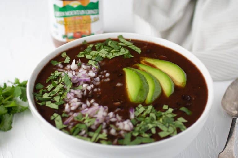 Easy black bean soup with avocado, cilantro, and red onion in a white bowl.