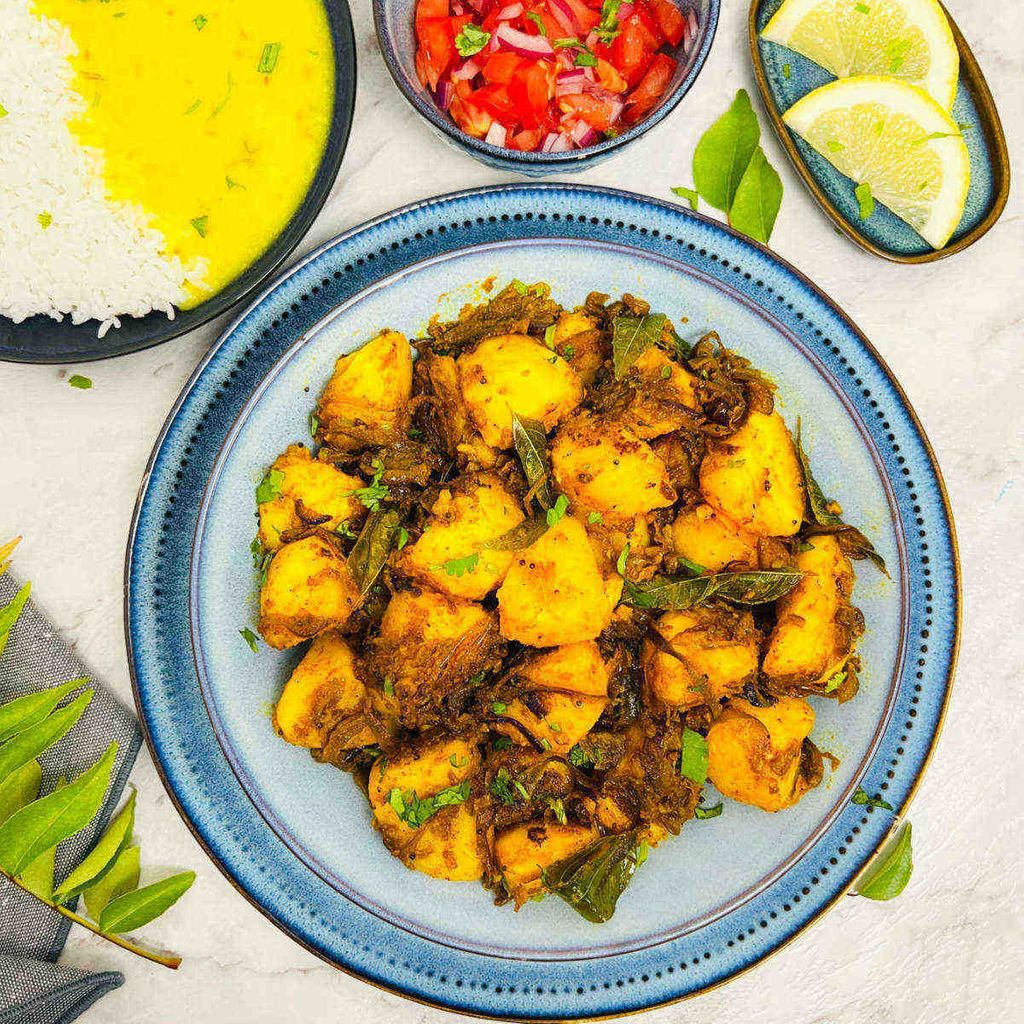 Bombay potatoes on blue plate with assortment of food in background.