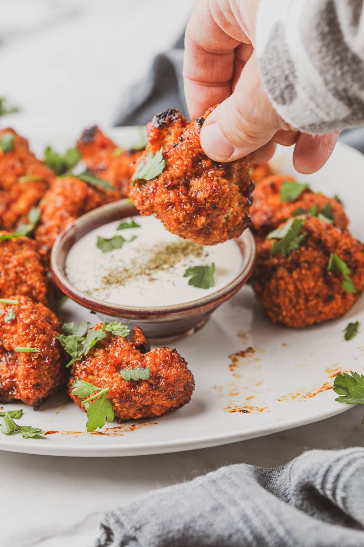 Crispy cauliflower bite in hand dipping into sauce.