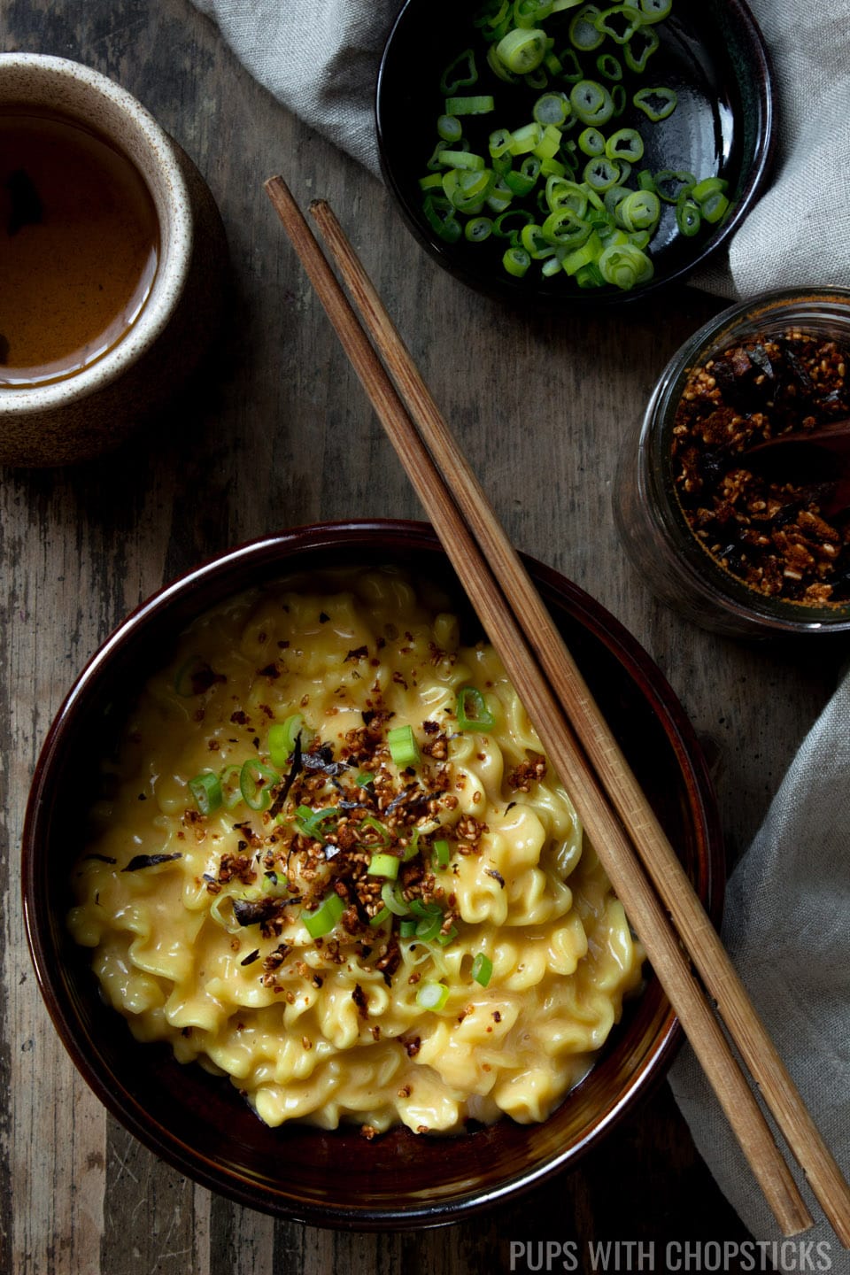 Cheese ramen in a bowl with chopsticks, bowl of furikake and scallions on the side.