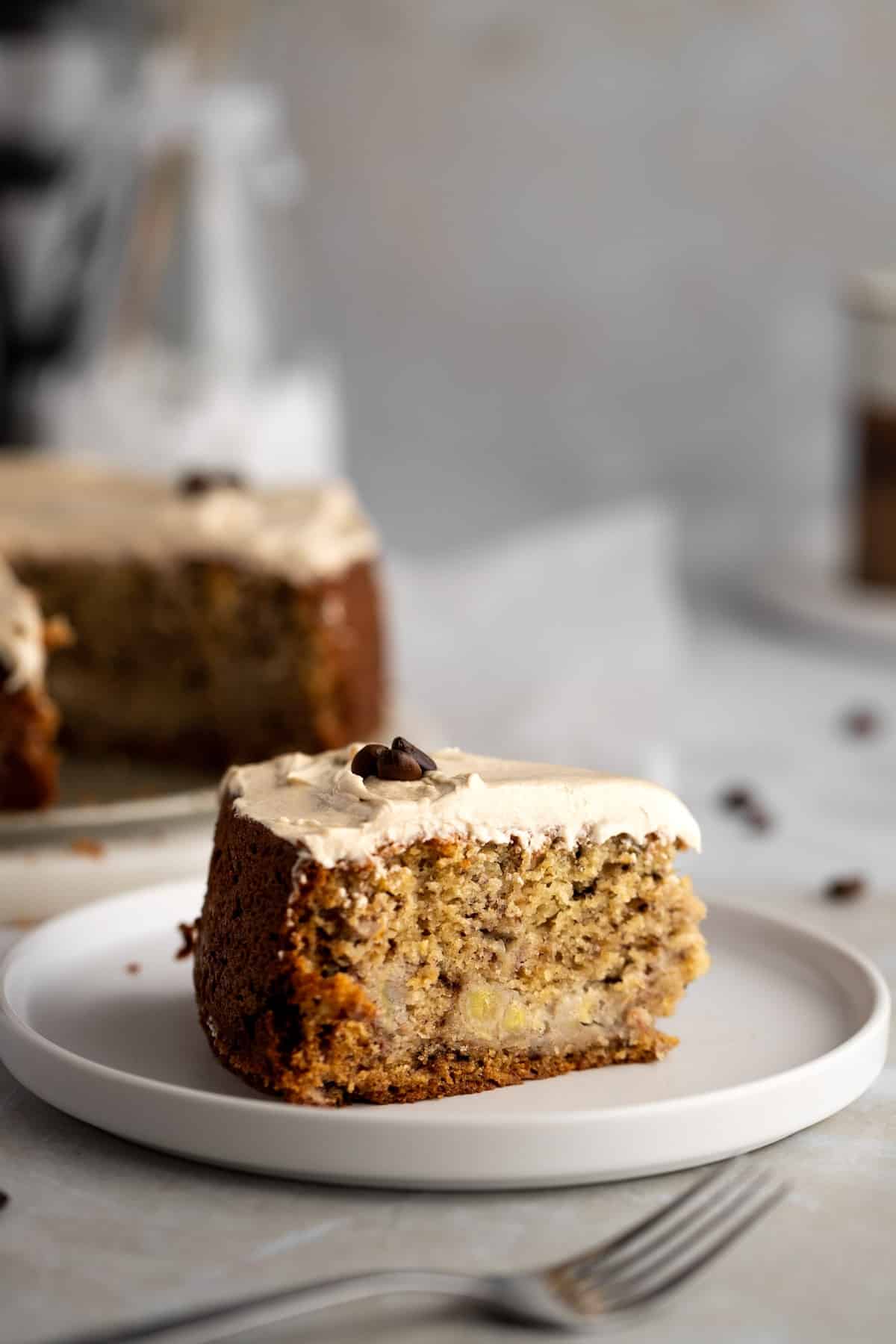 Coffee cake slice with espresso frosting on a saucer with rest of the cake in background.