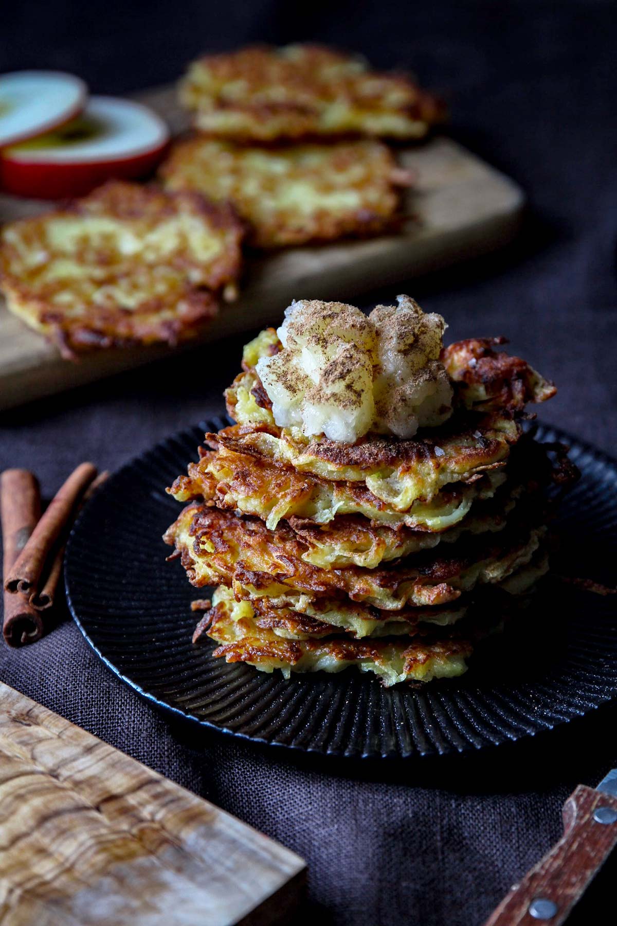 Stack of German pancakes on a black plate with cinnamon applesauce.