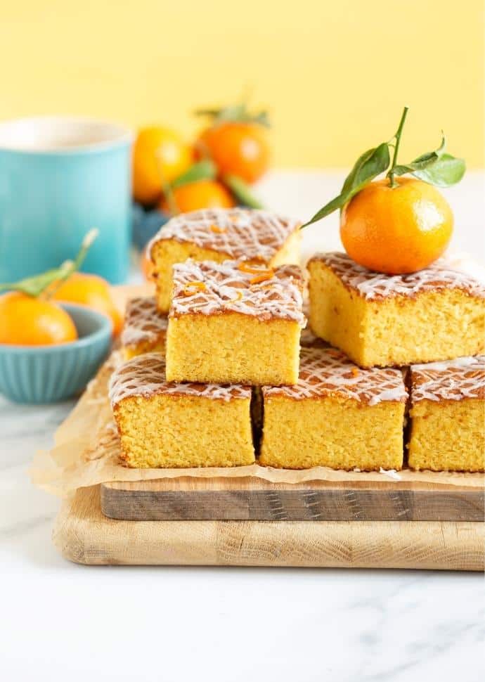 Clementine cake sliced and stacked on a wooden cutting board.