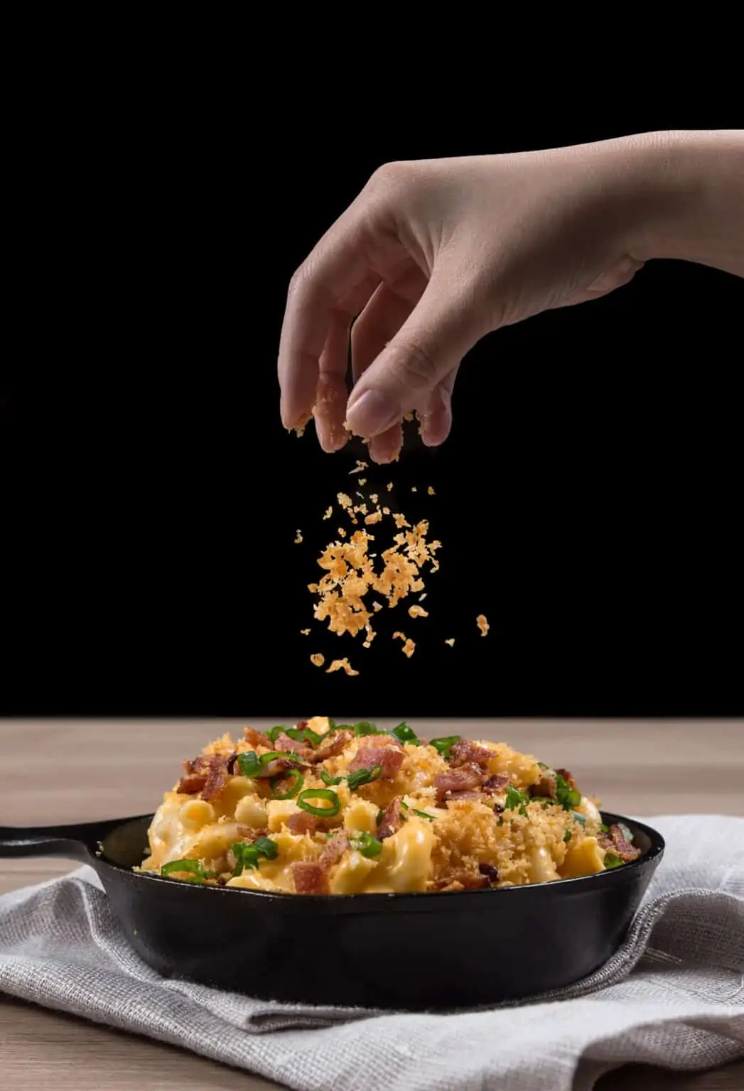 Hand sprinkling bread crumbs on loaded instant pot mac and cheese in a cast iron pan.