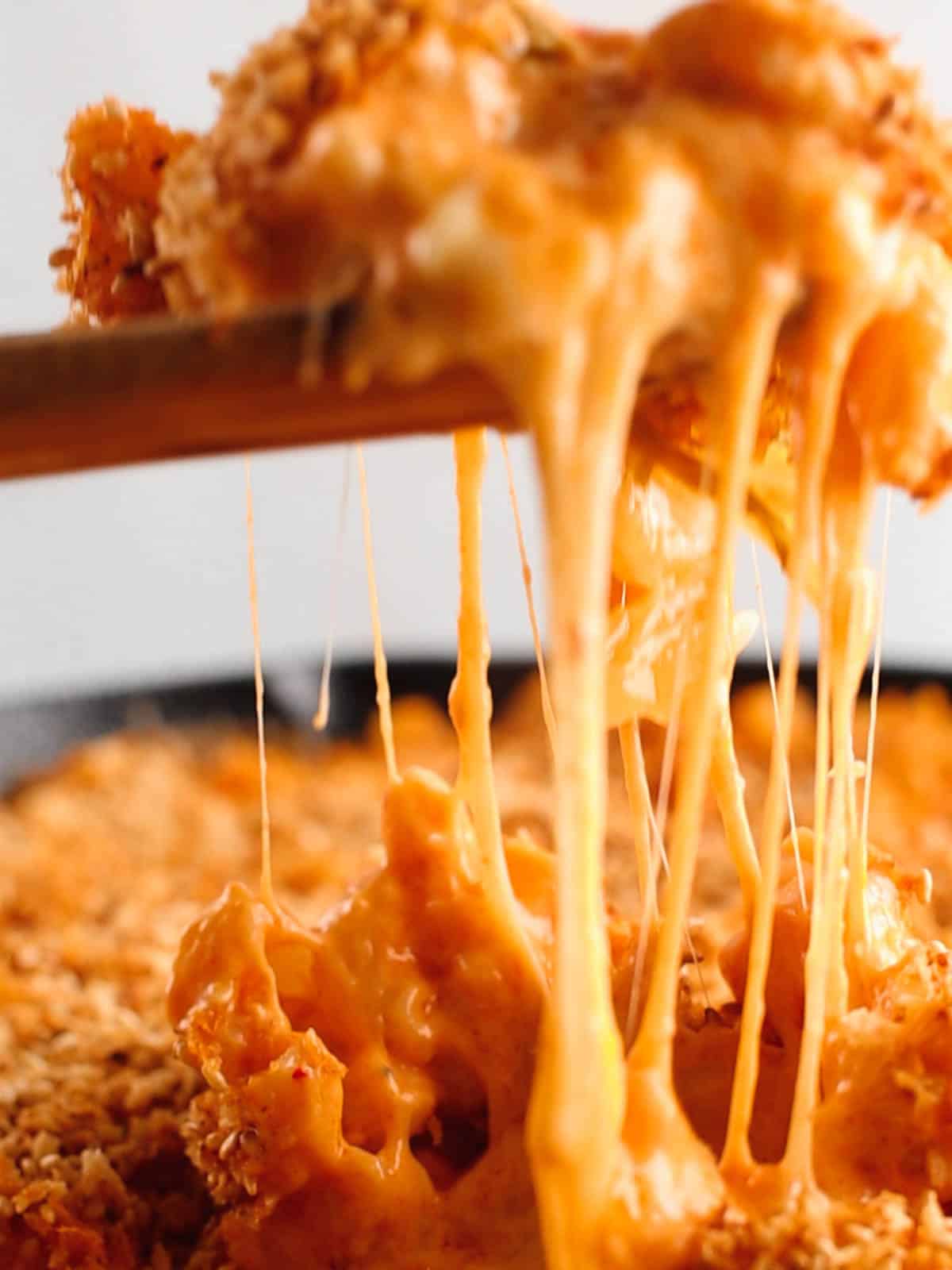 Cheese pull shot of kimchi mac and cheese in a wooden spoon.