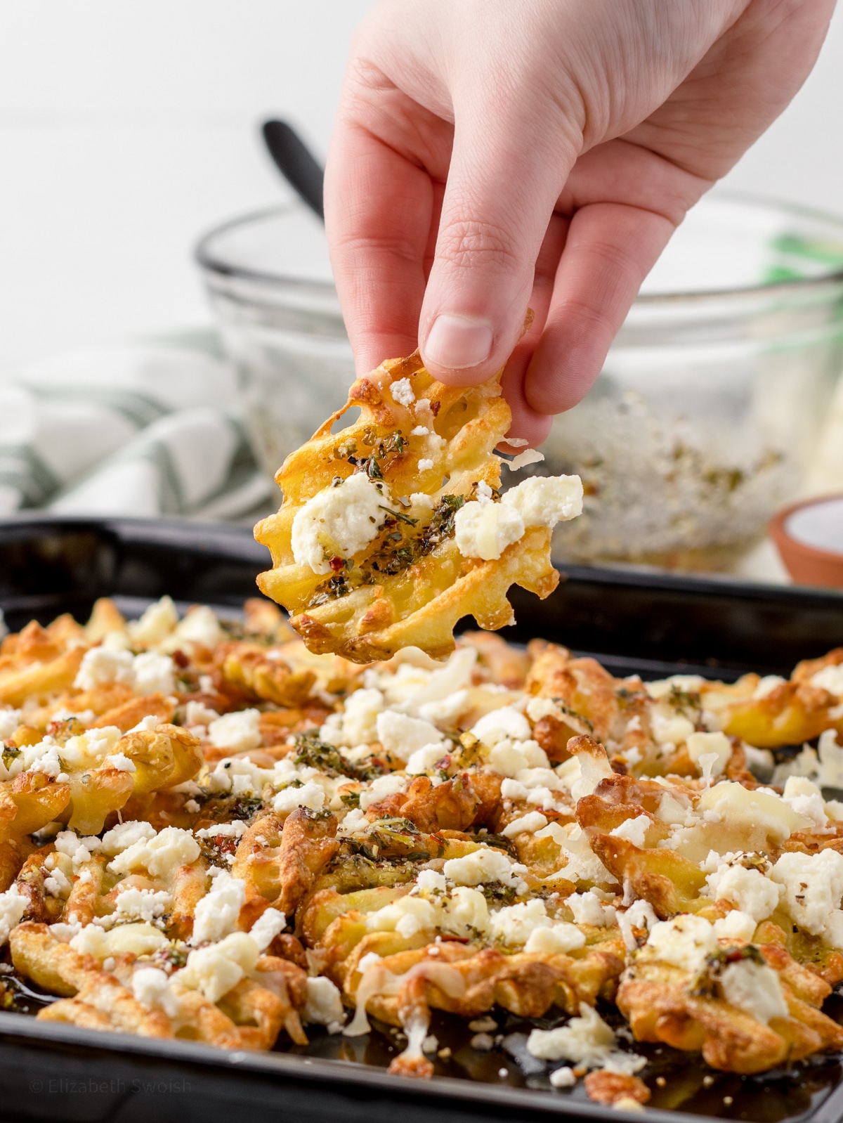 Hand grabbing lemon feta fries on baking tray.