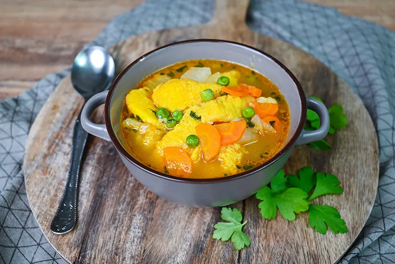 Mixed vegetable soup with dumplings in a bowl on a wooden cutting board.