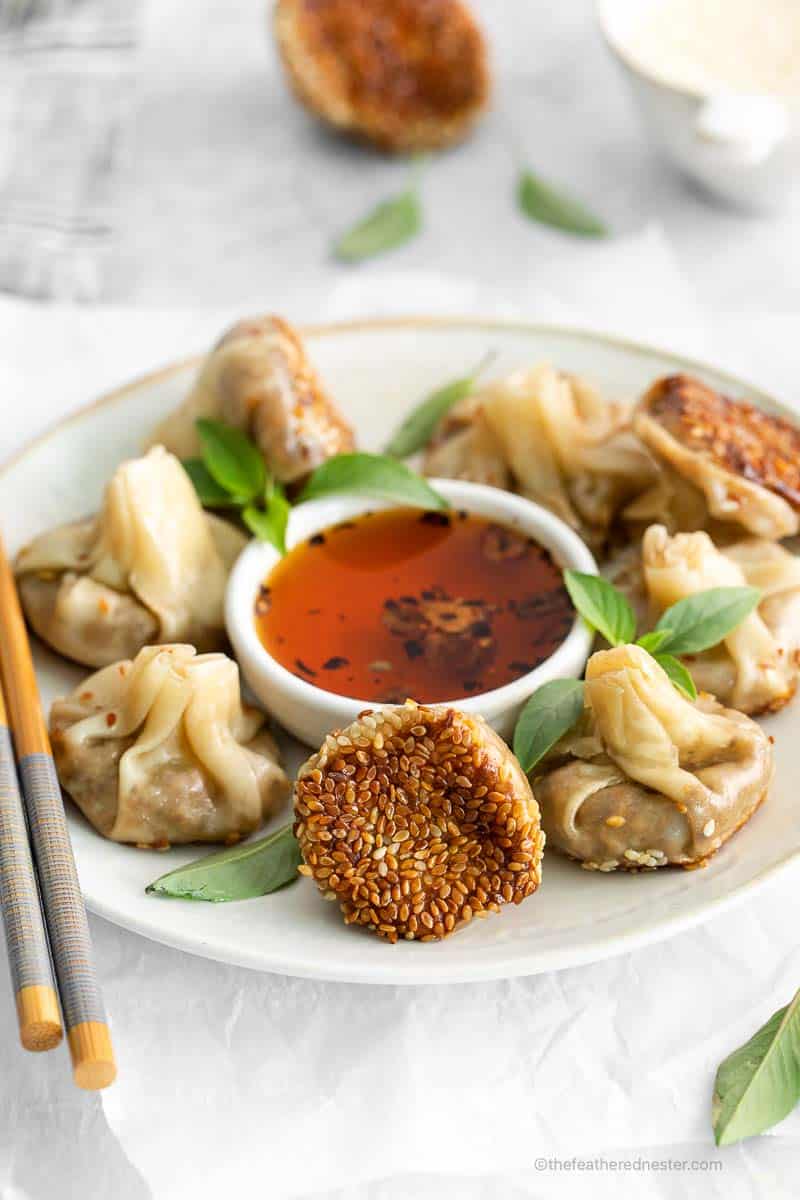 Mushroom dumplings with dipping sauce, on  a white plate with chopsticks.
