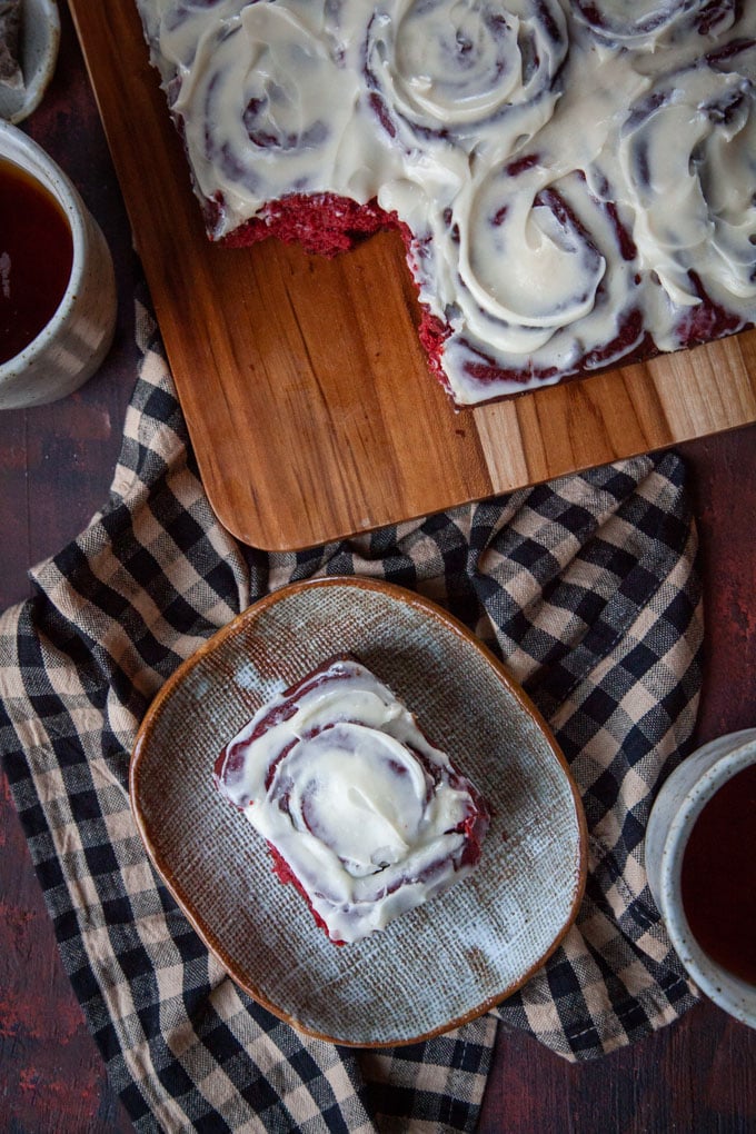 Red velvet cinnamon rolls on a wooden tray with one a plate.