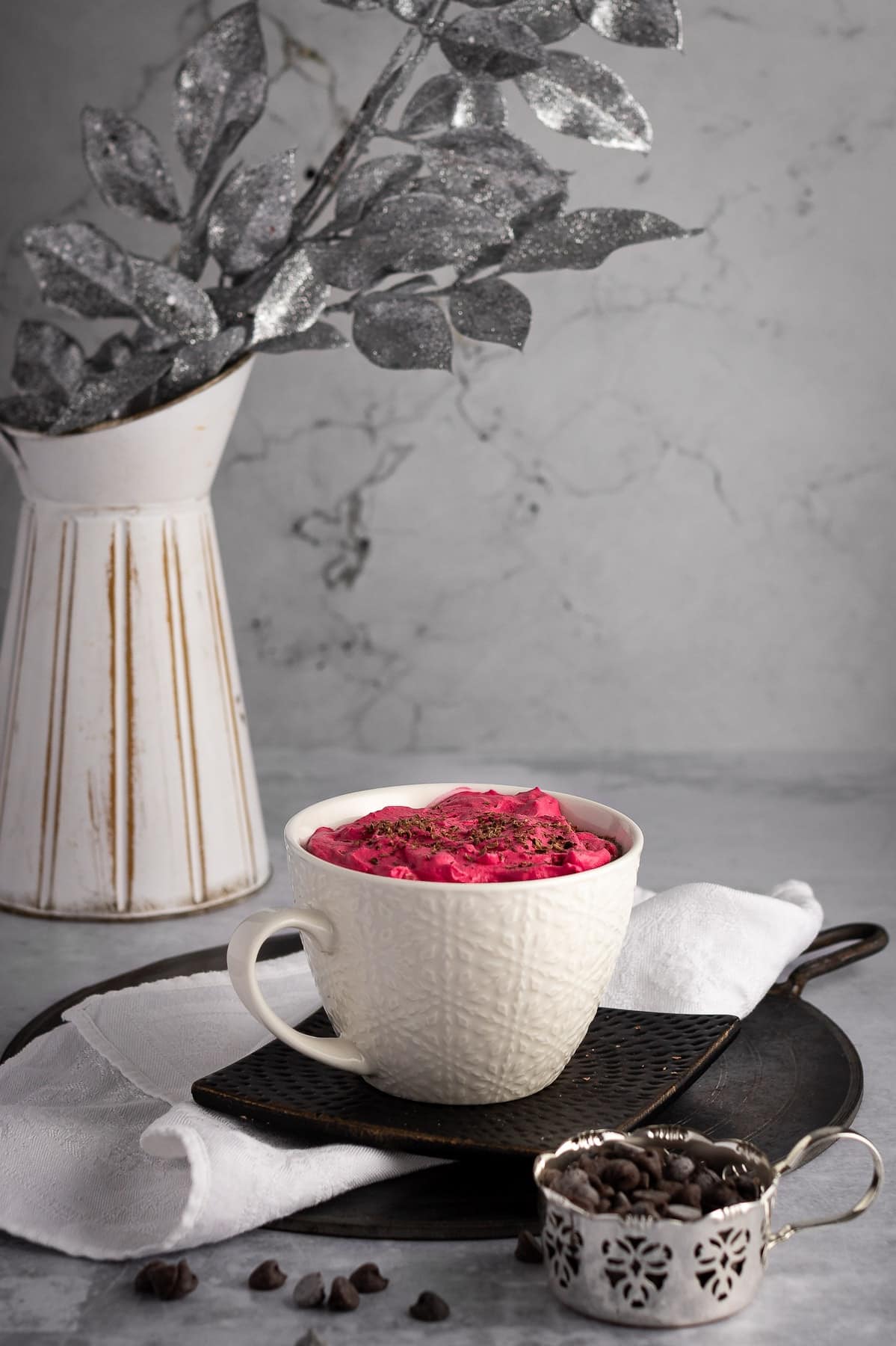 Red velvet latter in a white cup with chocolate chips in the foreground.