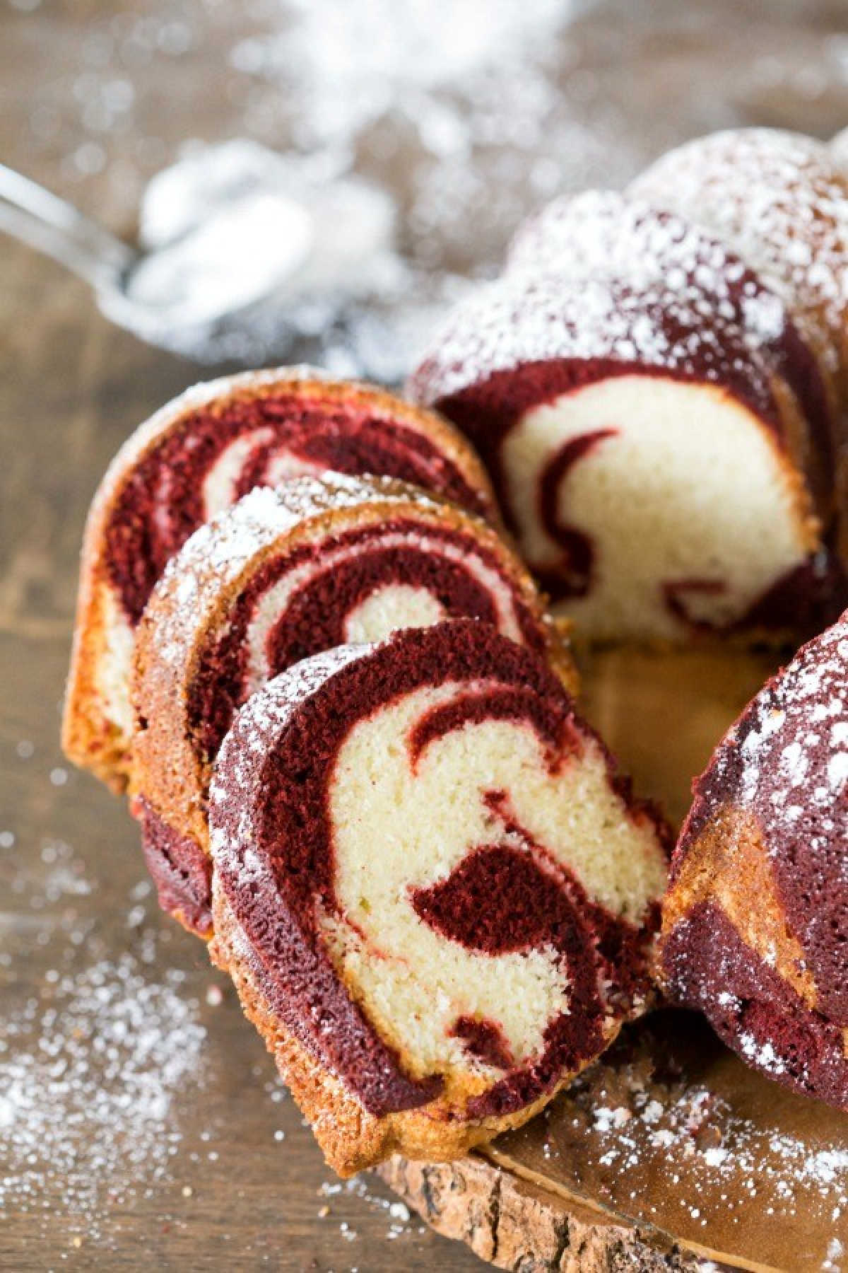 Sliced red velvet marble cake dusted with powdered sugar on a cutting board.