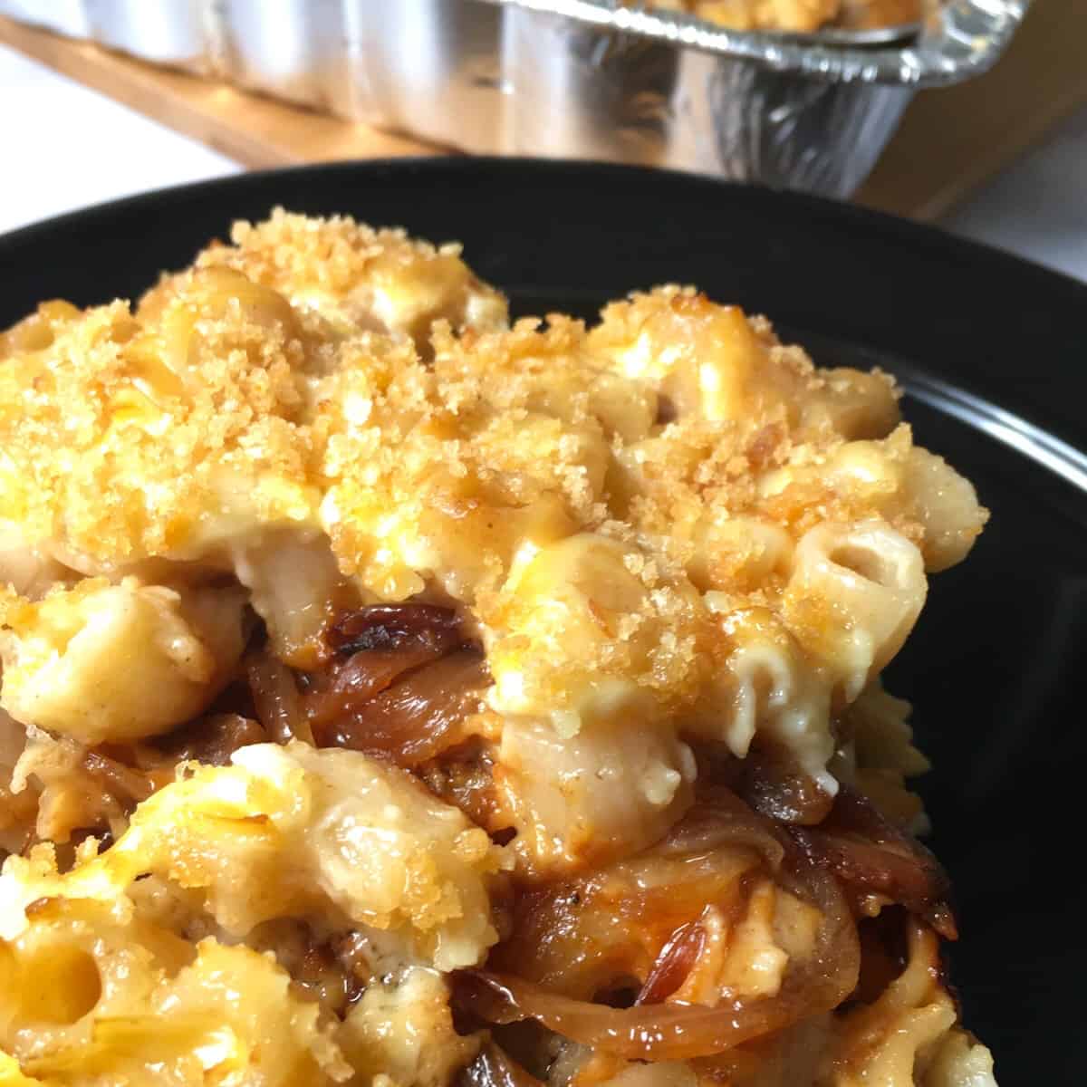 Smoked mac and cheese with caramelized onions on a black plate.