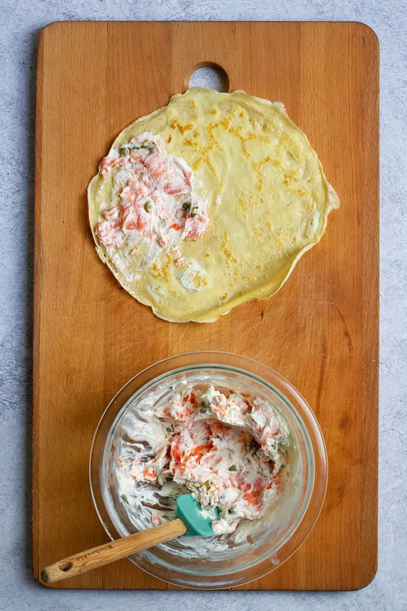 Smoked salmon crepes being assembled on a wooden cutting board.