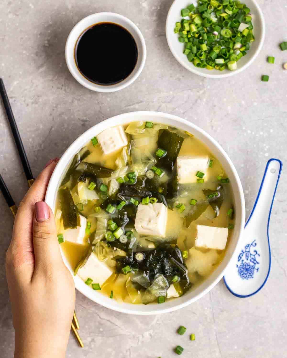 Hand grabbing Japanese wakame miso soup with cabbage.