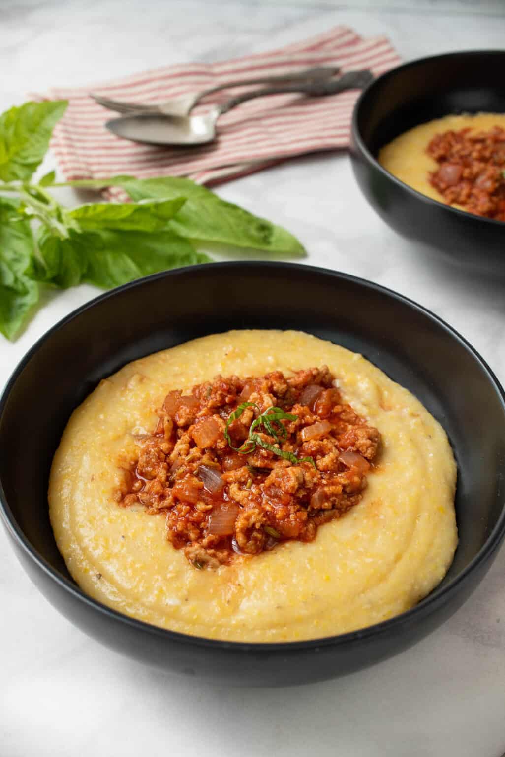 Bowl filled with three cheese polenta topped with ground turkey Italian sausage.