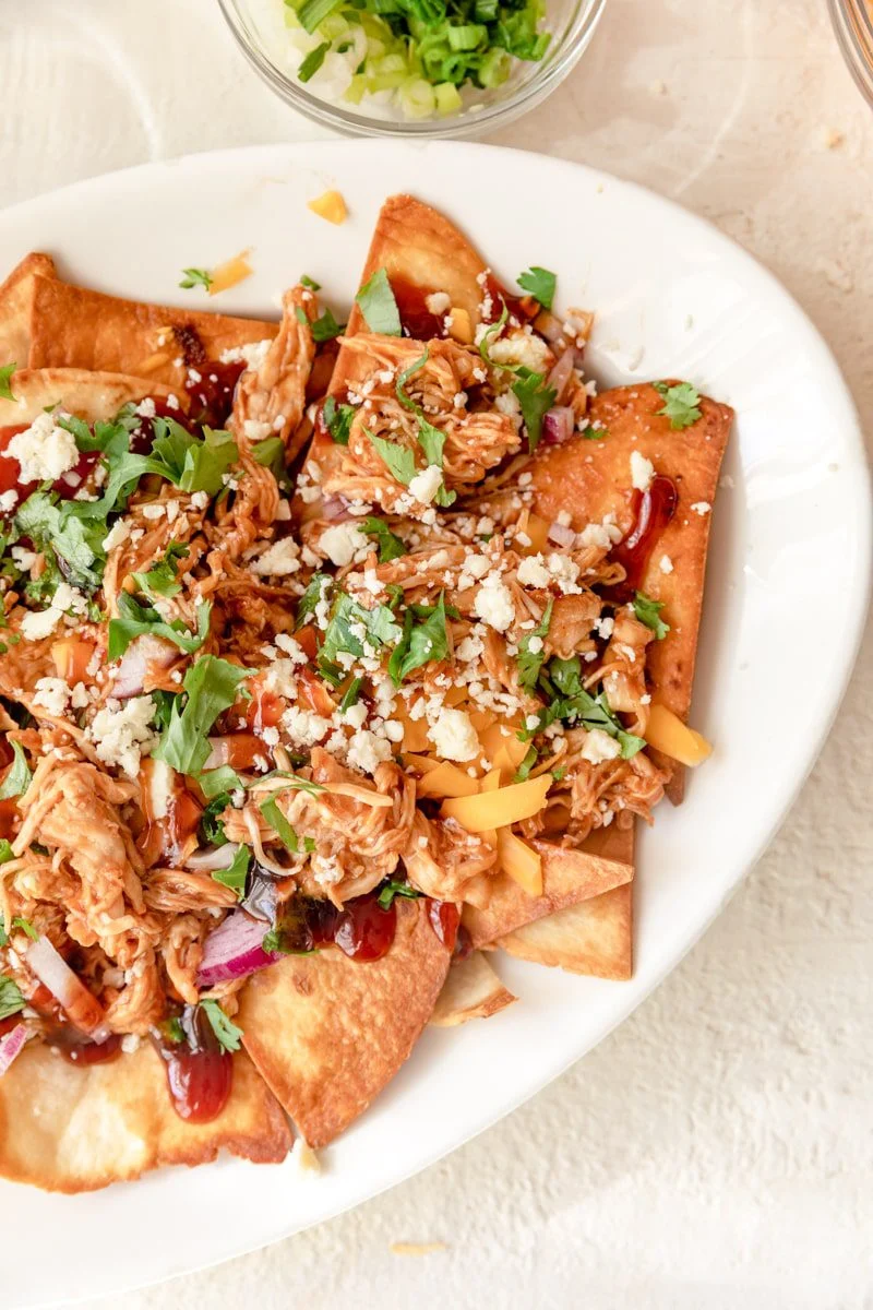 BBQ chicken nachos with all the fixings on a white plate.