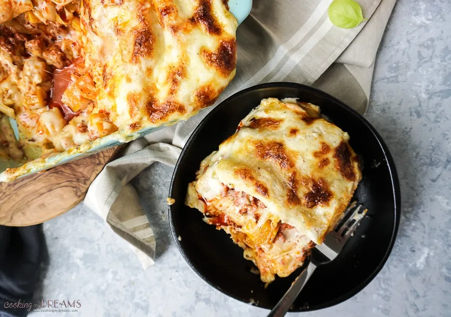 Butternut squash and sausage lasagna in a baking dish with a serving on a plate.