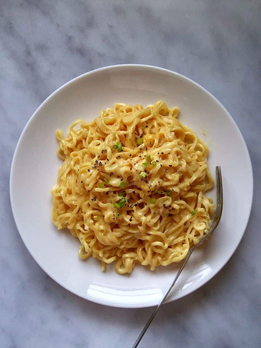 Cheese ramen noodles with scallions and black pepper on a white plate with a fork.