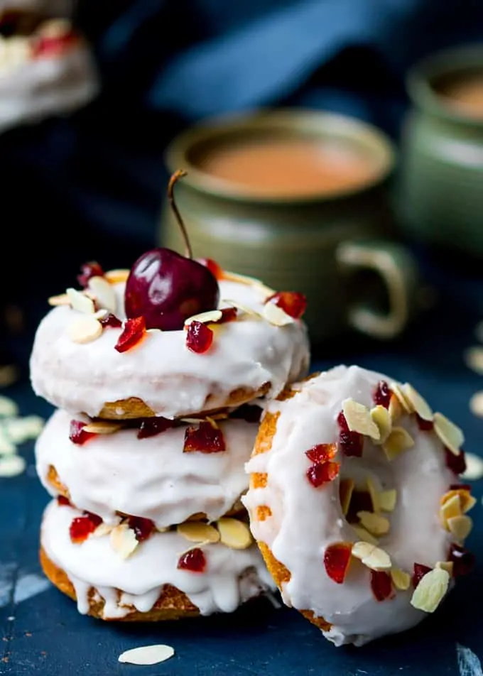 Stack of cherry Bakewell donuts with mugs of coffee in the background.