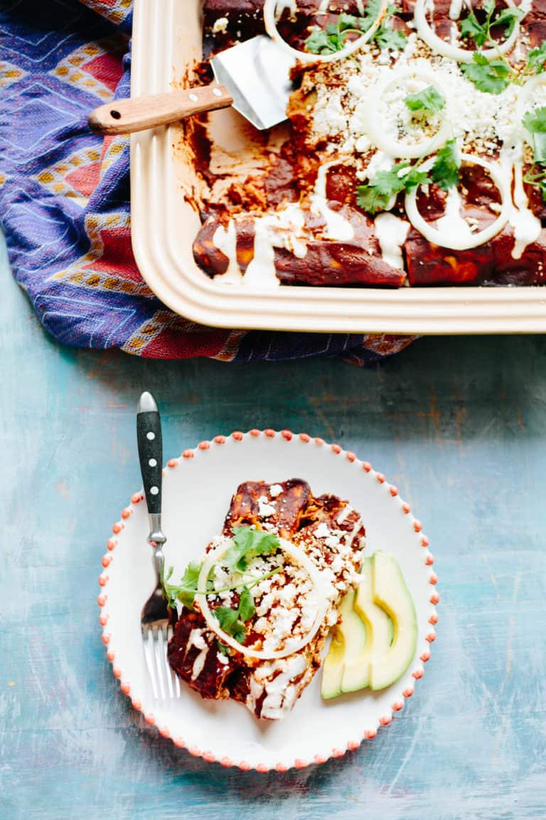 Mole enchiladas with avocado slices on a decorative white plate.