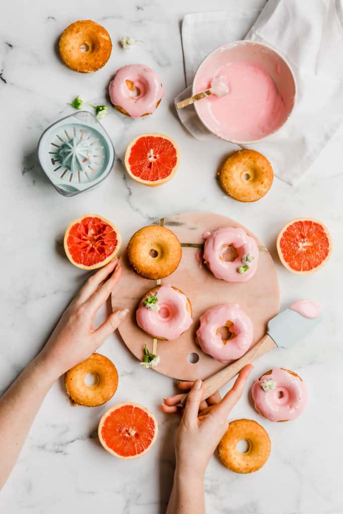 Grapefruit donuts on display with halved grapefruit, hands and spatula.